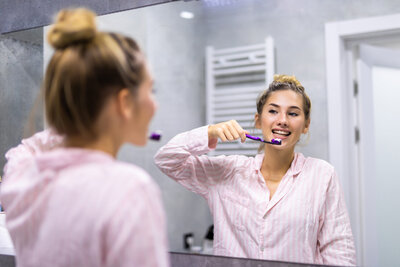 Beautiful young woman brushing teeth in front of her bathroom mirror.