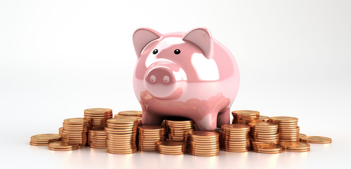A piggy bank stands on stacked coins against a white backdrop. O “porquinho” de moedas ainda é a melhor forma de incentivar a poupança